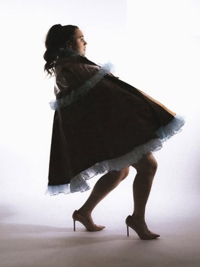 Model mid-turn in a dark cape with pale blue ruffle trim